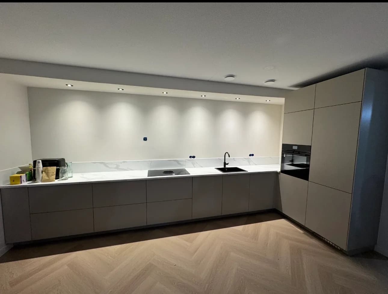 Afgemonteerde greeploze keuken in greige met marmerlook werkblad en achterwand, hoge kastenwand met inbouwoven